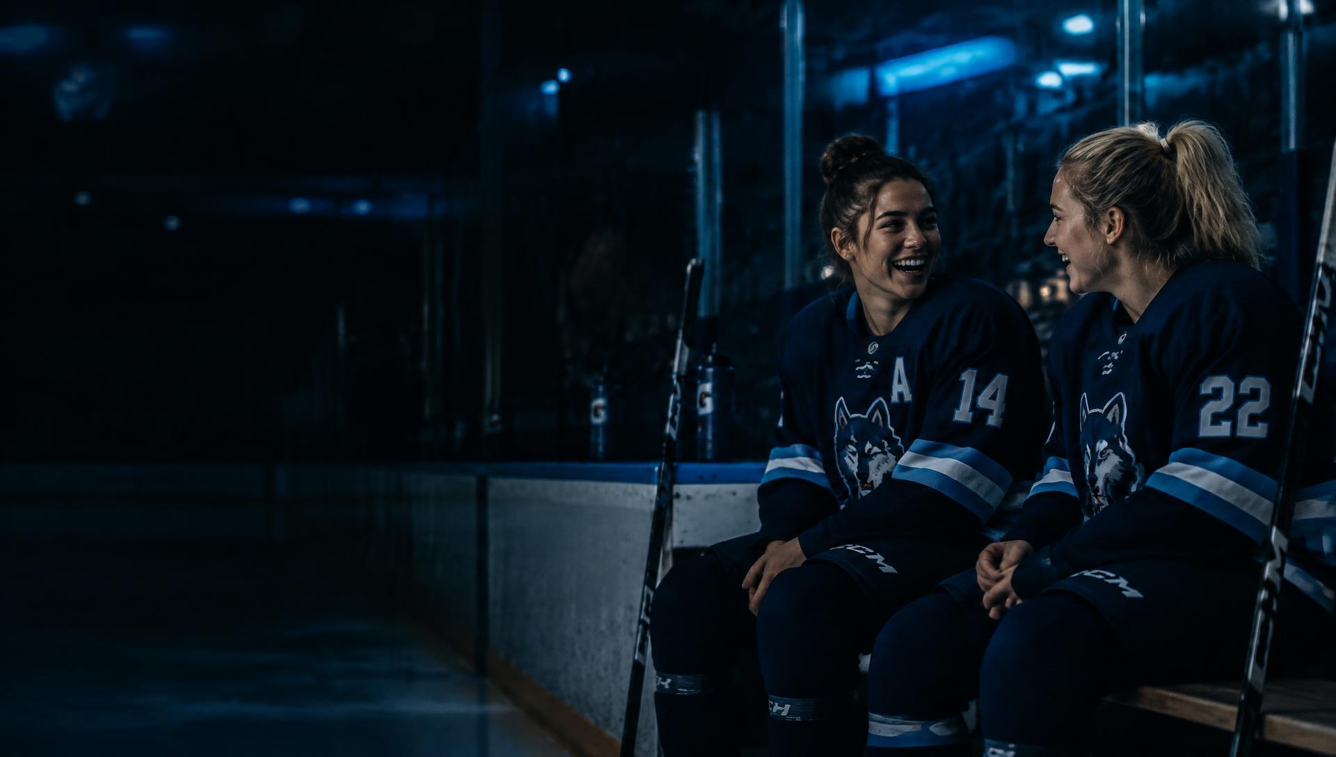 Two female hockey players laughing on the bench